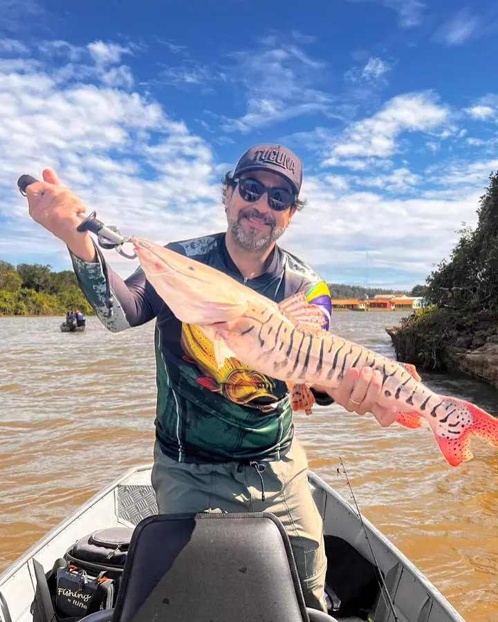 Pescador sorridente segurando um peixe no barco, com camiseta personalizada