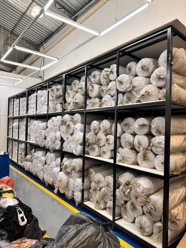 Estoque com dezenas de rolos de tecido organizados em prateleiras