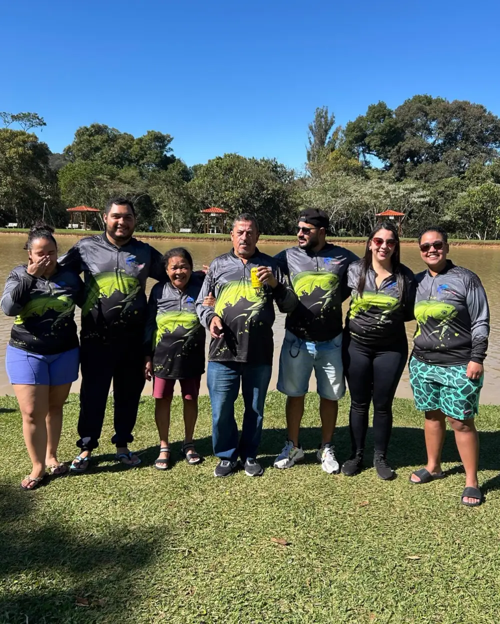 Família reunida à beira de um lago com camisetas de pesca pretas e verdes