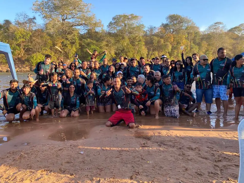 Dezenas de pescadores com camisetas verdes iguais reunidos na praia de um rio ao pôr do sol