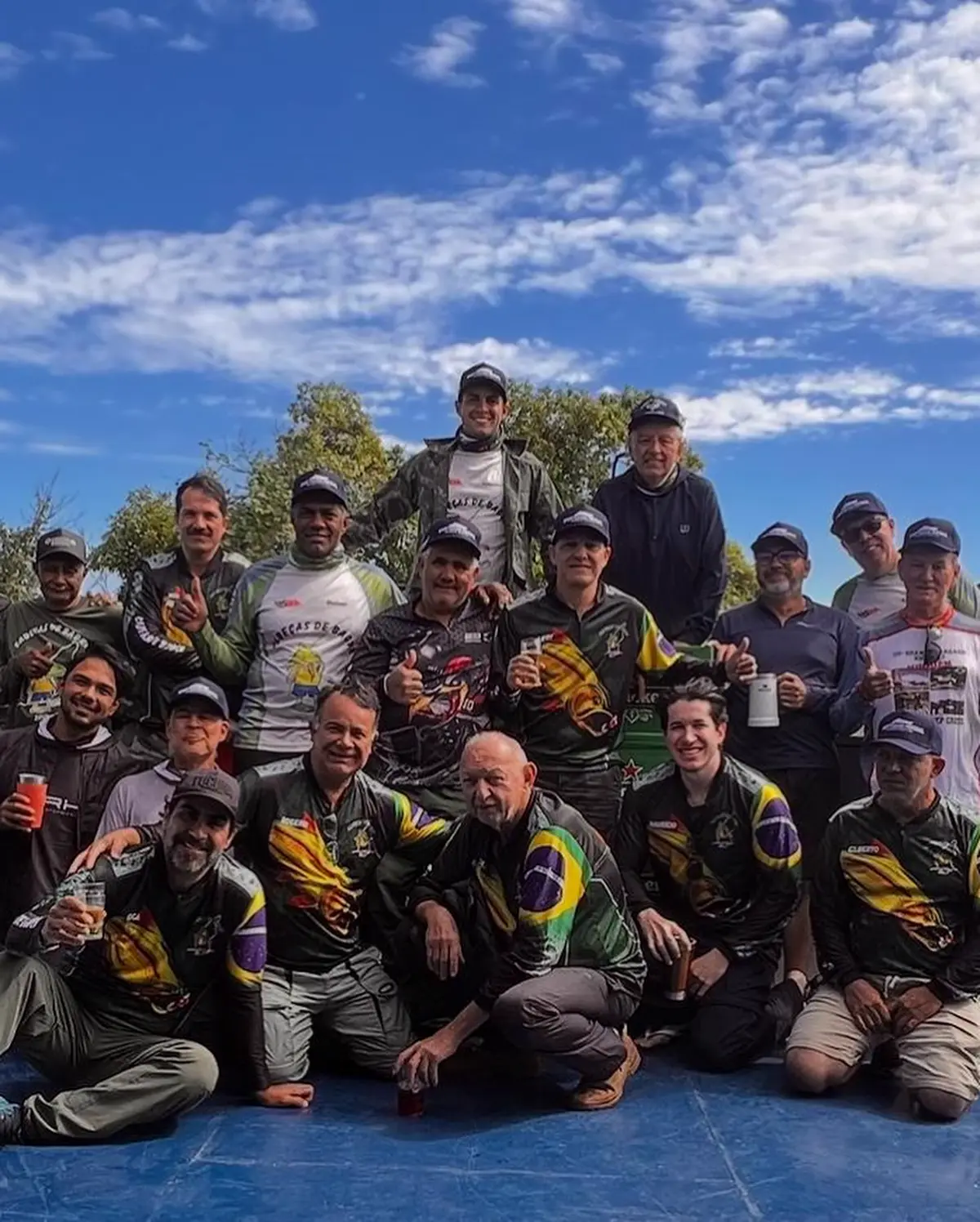Grupo de pescadores sob céu azul vestindo camisetas personalizadas com bandeira do Brasil nas mangas
